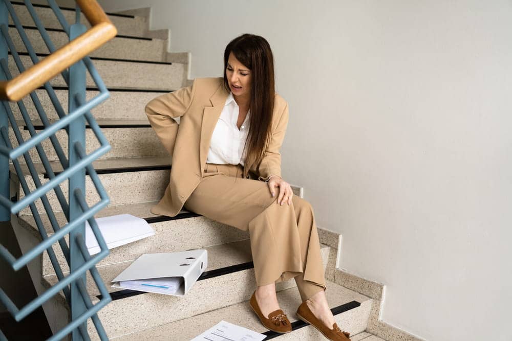 Image is of a woman sitting on a staircase after a fall, concept of a premises liability lawyer helping victims injured by hazardous property conditions.