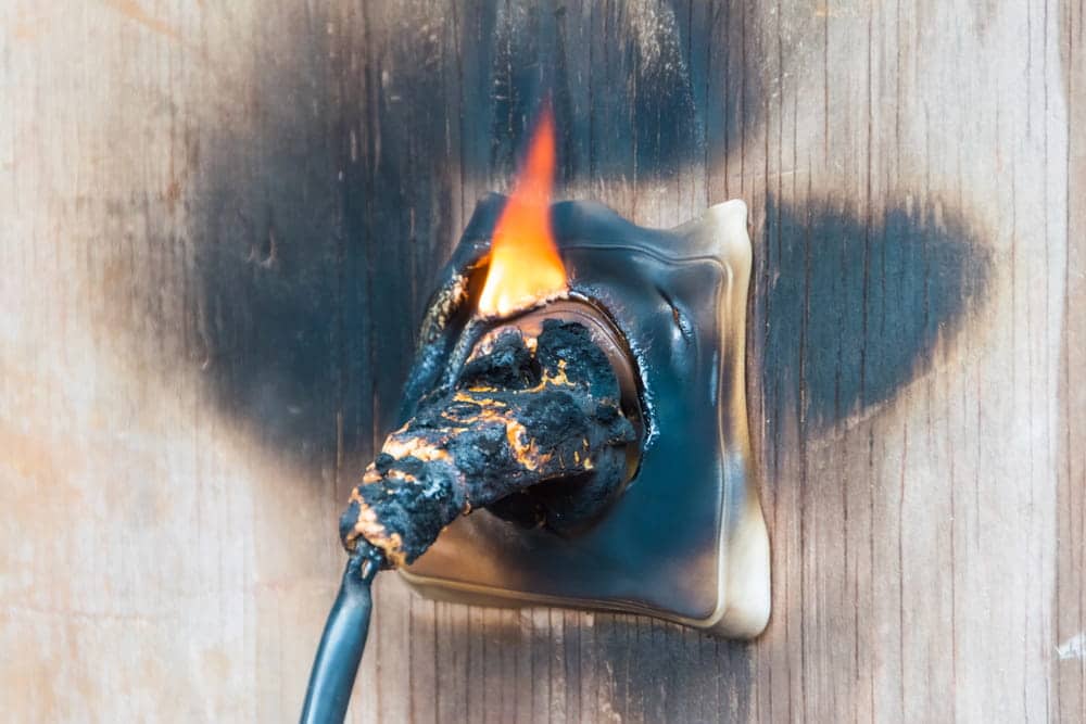 Image is of a burned electrical outlet with flames and heat damage, concept of an Aiken product liability lawyer handling claims involving defective electrical products.