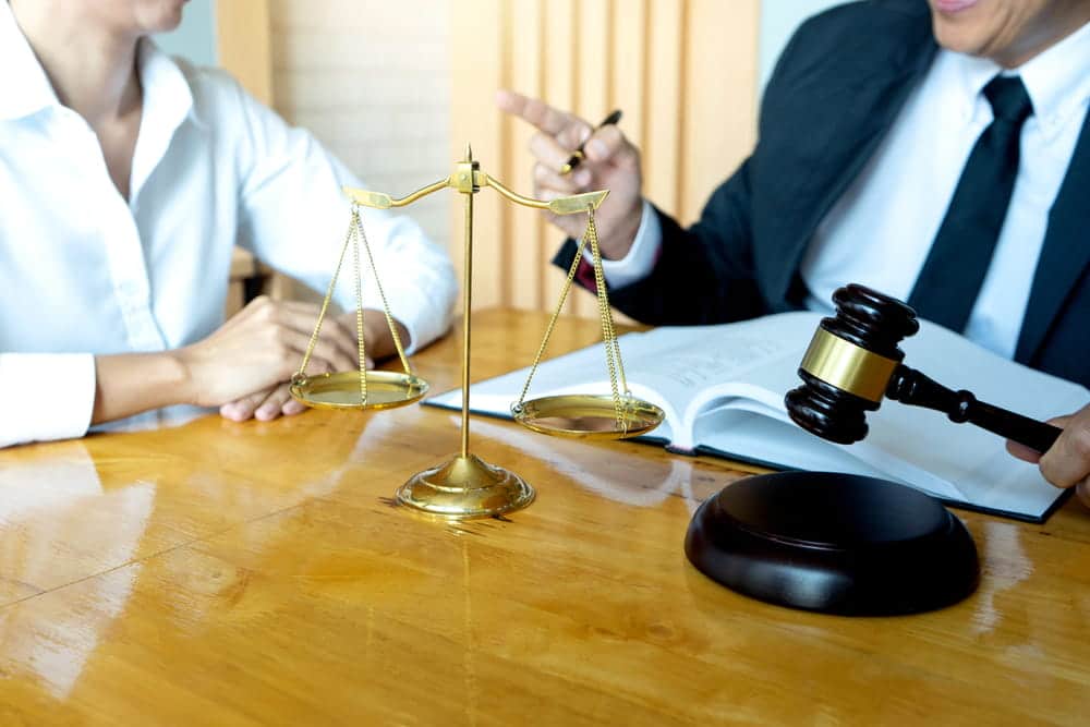 Image is of legal professionals discussing case details at a conference table with scales of justice, concept of an Aiken rape lawyer preparing a defense strategy.