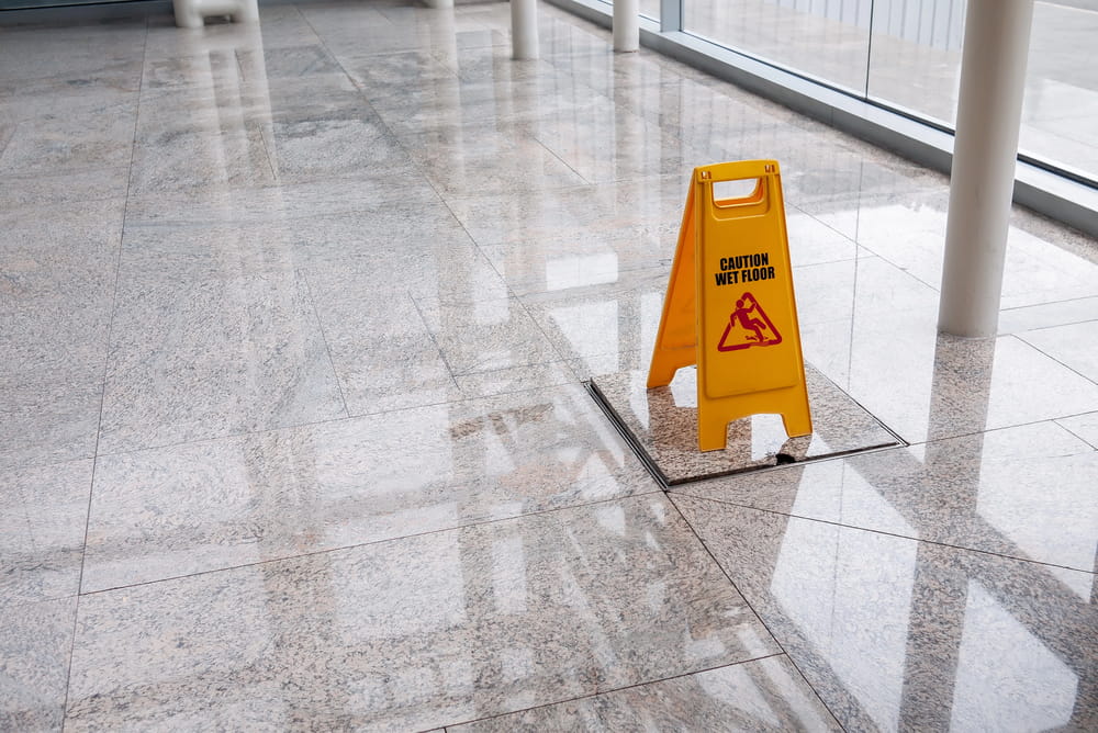 Image is of a wet floor warning sign on a polished surface, concept of a slip and fall lawyer investigating hazardous property conditions.