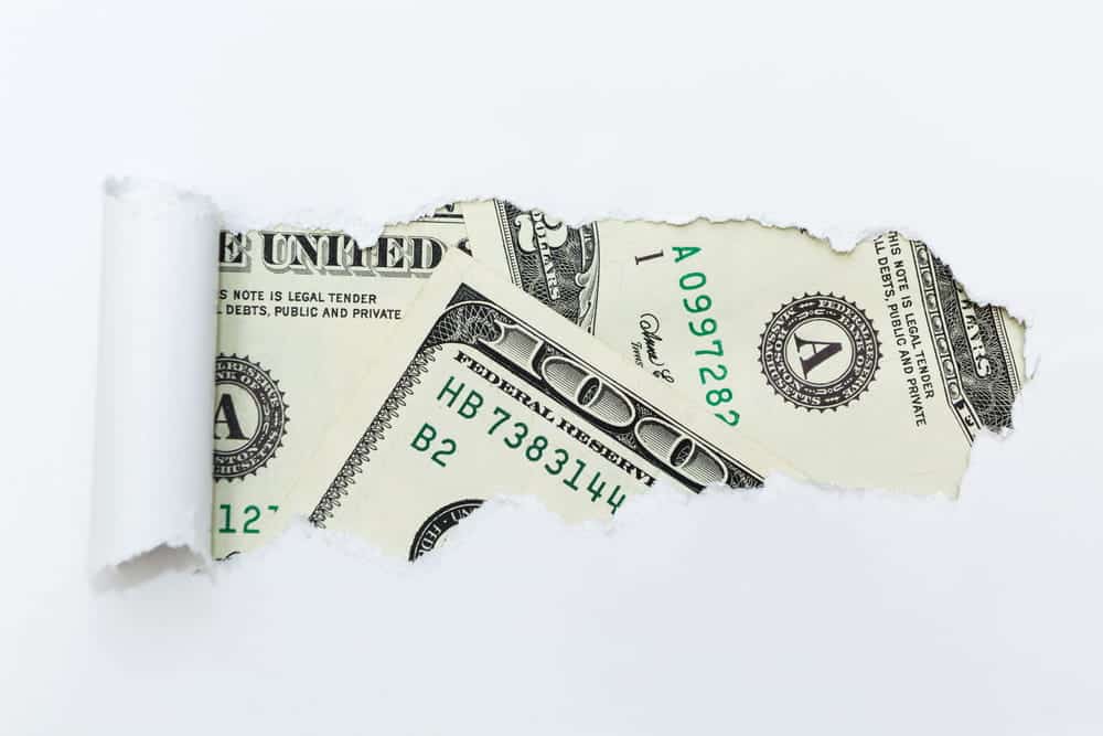 Image is of U.S. currency visible through torn paper, concept of an Aiken tax evasion lawyer handling cases involving hidden income and financial investigations.