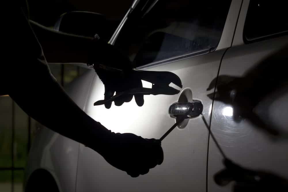 Image is of an individual using tools to gain access to a vehicle at night, concept of an Aiken theft lawyer defending against auto theft allegations.