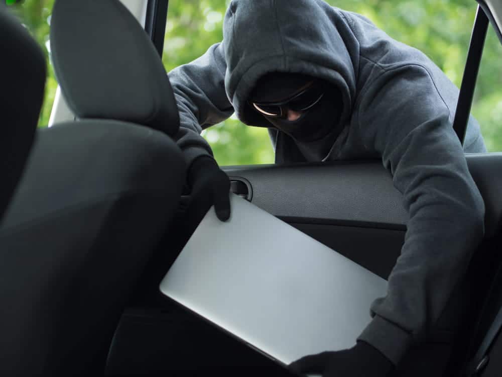 Image is of an individual removing a laptop from a vehicle, concept of an Aiken theft lawyer representing clients facing vehicle theft charges.