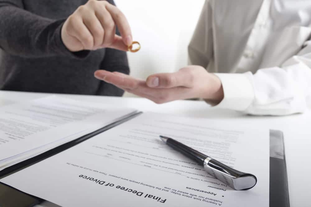 Image is of spouses exchanging a wedding ring above divorce documents, concept of finalizing terms with an uncontested divorce lawyer in Aiken.
