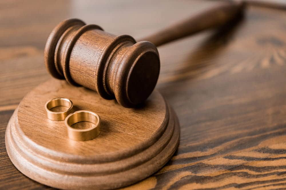 Image is of a judge's gavel and wedding rings on a wooden surface, concept of resolving a marriage through an uncontested divorce lawyer in Aiken.