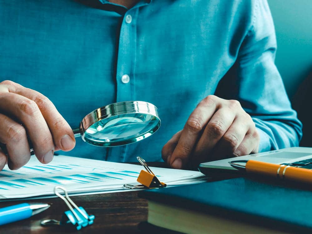 Image is of an individual reviewing financial documents with a magnifying glass, concept of Aiken white collar crime defense helping clients facing fraud and financial crime investigations.