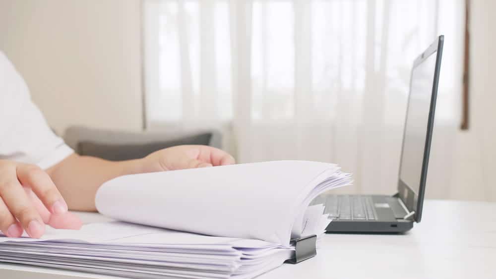 Image is of an individual reviewing a stack of records and documents, concept of a wrongful death lawyer examining evidence and case materials.