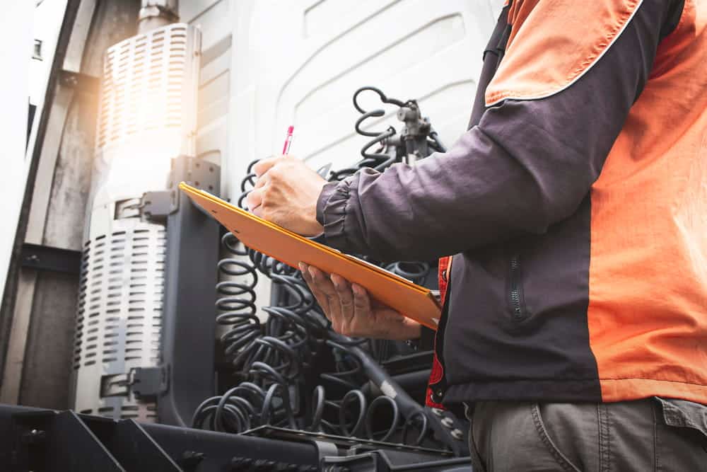Image is of a commercial vehicle inspector recording information on a clipboard, concept of vehicle inspections and maintenance records supporting a truck accident claim.