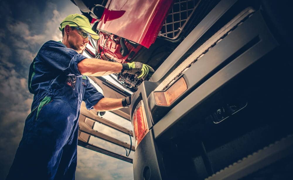Image is of a mechanic inspecting and repairing a commercial truck engine, representing maintenance issues that can contribute to truck accidents in Aiken.