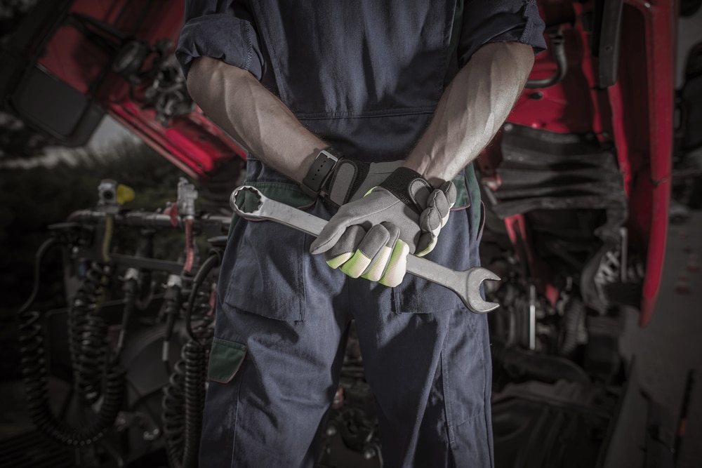 Image is of a commercial truck mechanic holding a wrench during a vehicle inspection, illustrating repair work related to preventing truck accidents in Aiken.