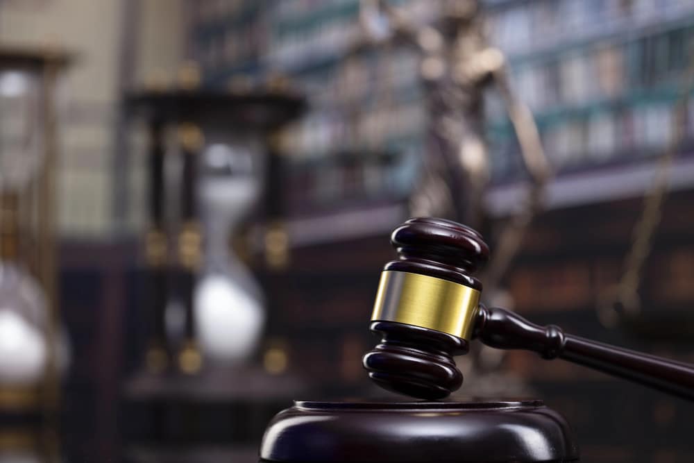 Image is of a courtroom gavel with a law library and hourglass in the background, concept of a criminal defense lawyer protecting legal rights and guiding clients through the criminal justice process.