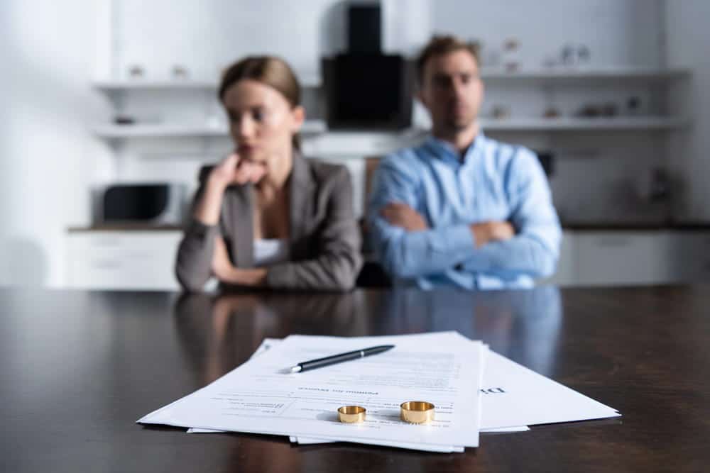 Image is of a separated couple sitting behind divorce documents and wedding rings on a table, concept of consulting a divorce lawyer in Aiken SC.