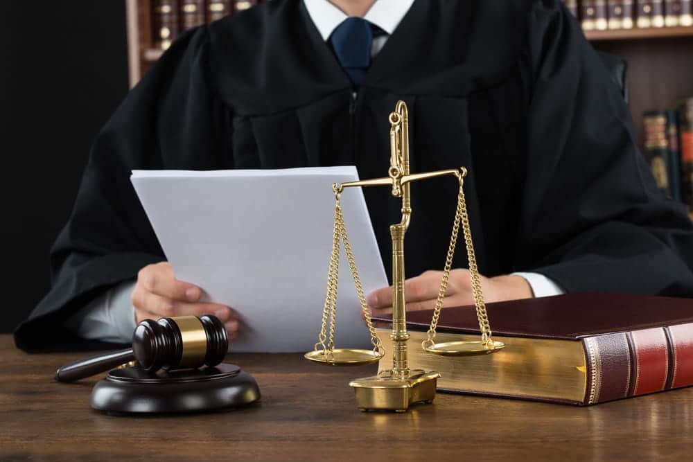Image is of a judge reviewing court documents with scales of justice on the desk, concept of DV charges in Aiken.
