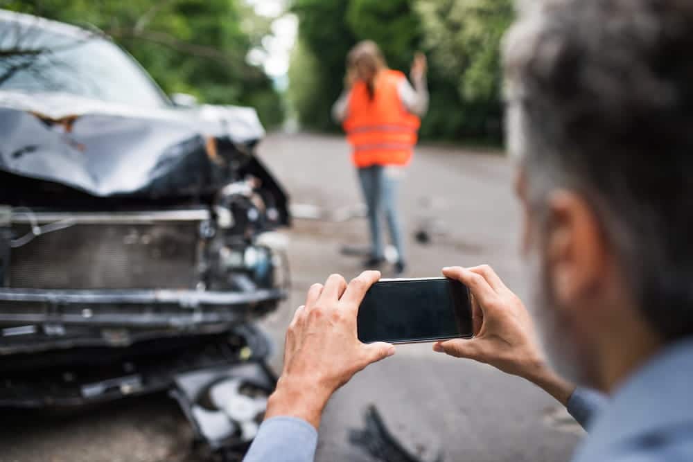 Image is of a person taking photographs of a damaged vehicle after a car accident in Aiken, concept of preserving evidence for an insurance claim.