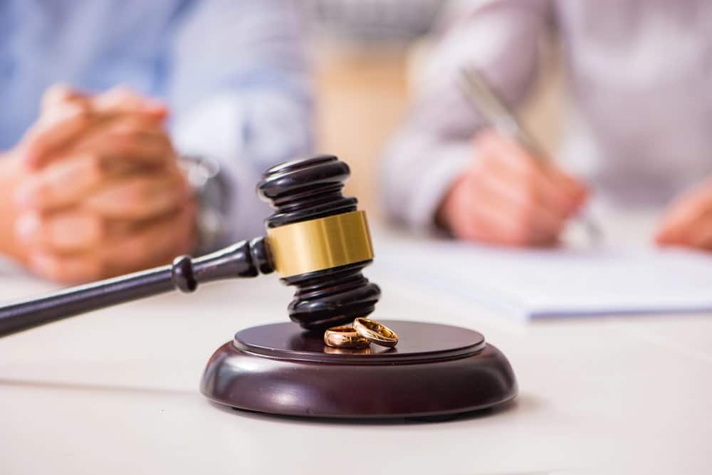 Image is of a judge's gavel and wedding rings with a couple signing legal documents, concept of divorce court proceedings in South Carolina.