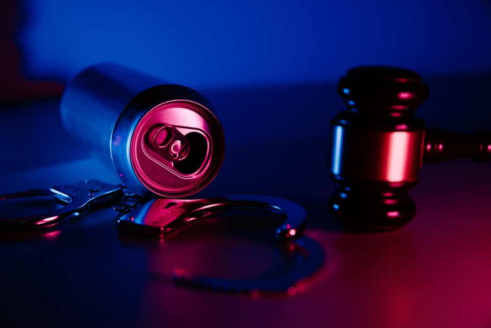 Image is of handcuffs, a gavel, and an opened beverage can, concept of prior DUIs and repeat DUI criminal proceedings in Aiken.