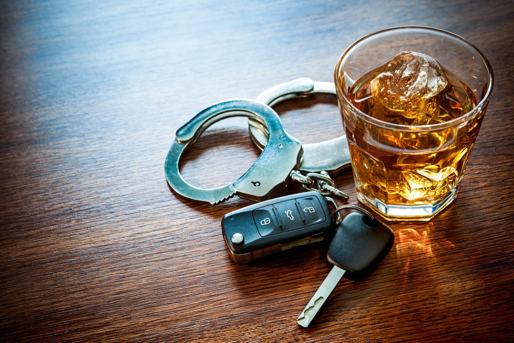 Image is of a glass of alcohol, vehicle keys, and handcuffs, concept of prior DUIs leading to increased penalties in Aiken.