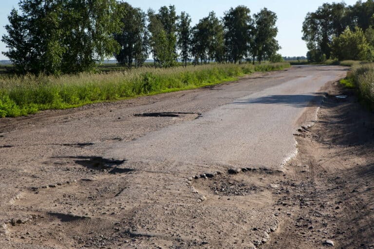 Image is of a rural roadway with multiple potholes and uneven pavement, concept of motorcycle accidents in Aiken caused by dangerous road surface conditions.