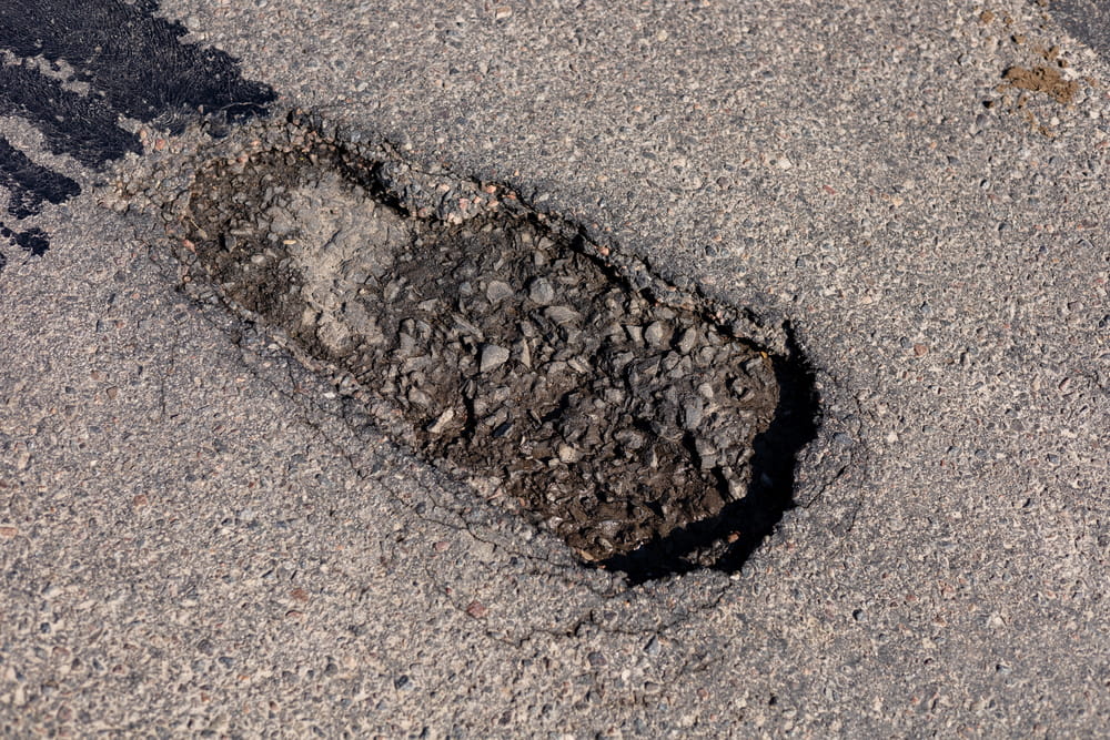 Image is of a deep pothole in the middle of a paved road, concept of motorcycle accidents in Aiken resulting from hazardous pavement defects.