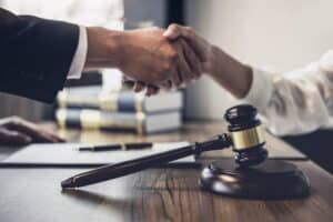 Image is of two people shaking hands across a desk with a gavel in the foreground, concept of a bike accident settlement reached through successful legal negotiations.
