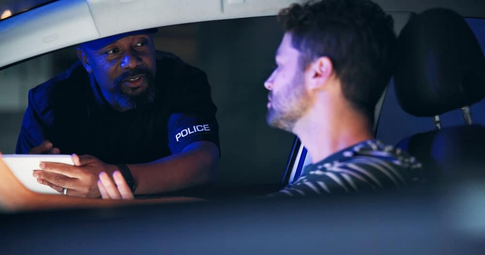 Image is of a police officer speaking with a driver during a traffic stop, concept of drugs in a shared car investigation in Aiken.