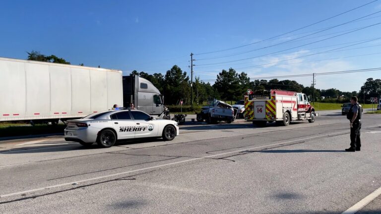Image is of emergency responders, a sheriff's vehicle, and a commercial truck at a crash scene, concept of a truck accident in Aiken involving insurance investigations.