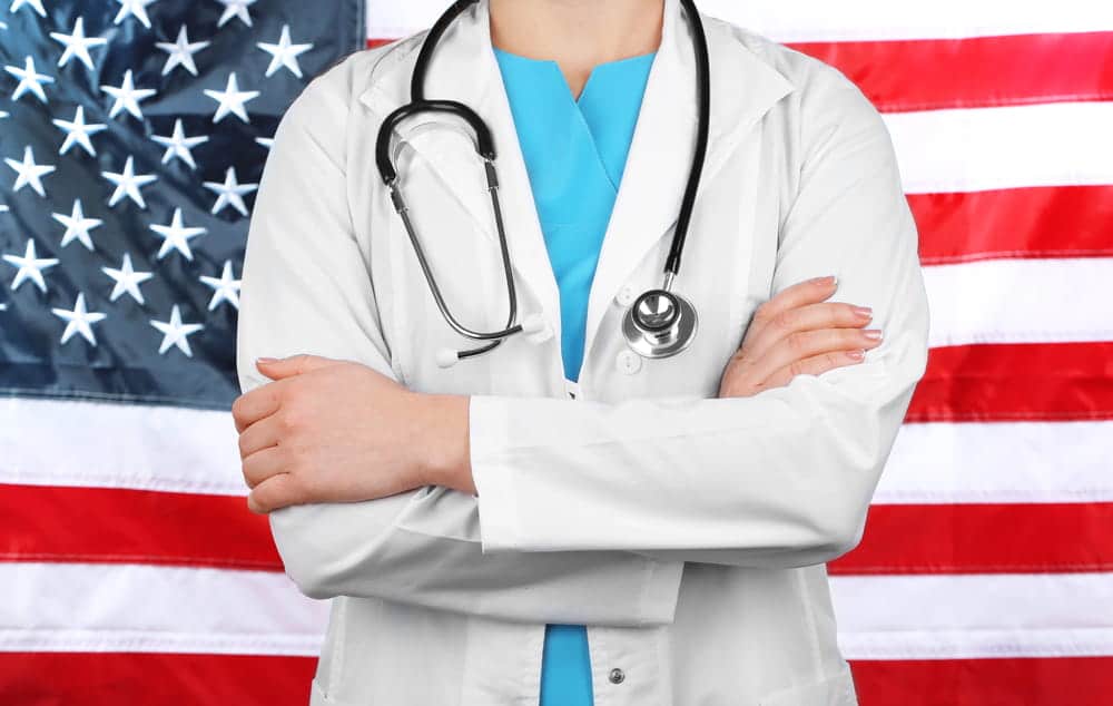 Image is of a licensed medical professional standing before an American flag, concept of a DV arrest affecting a professional license in Aiken