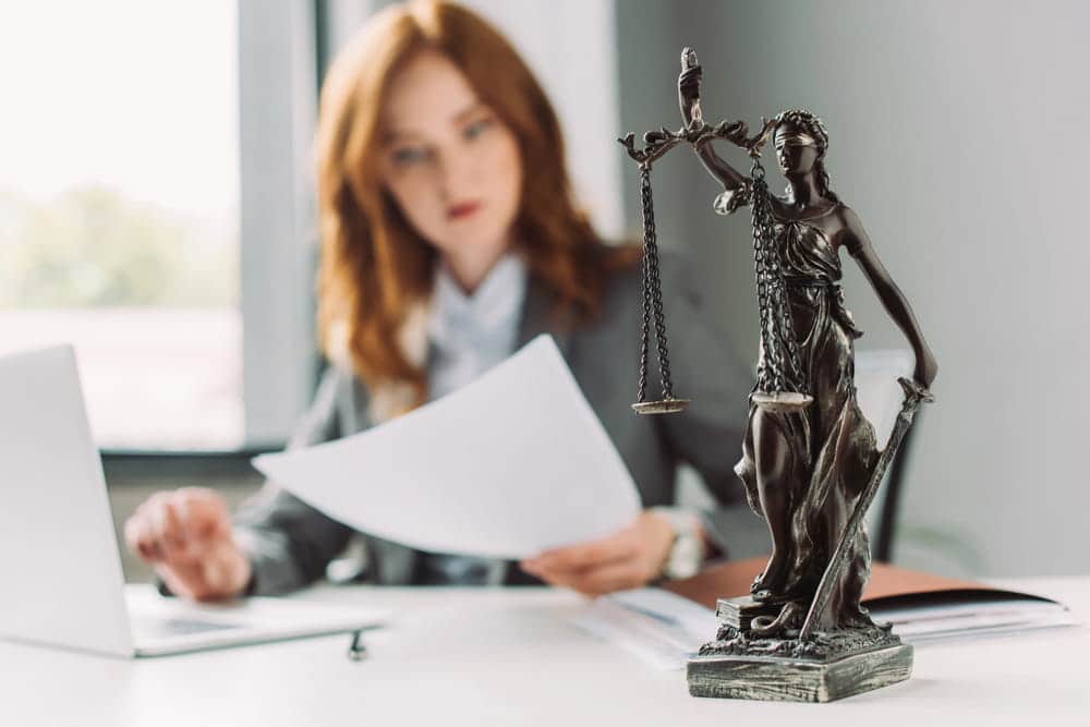 Image is of a lawyer reviewing legal documents beside a Lady Justice statue, concept of the adoption process and legal case preparation.