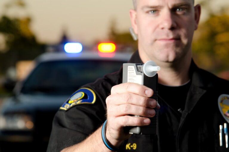 Image is of a police officer holding a breathalyzer near a patrol vehicle, concept of a failed breath test in Aiken.