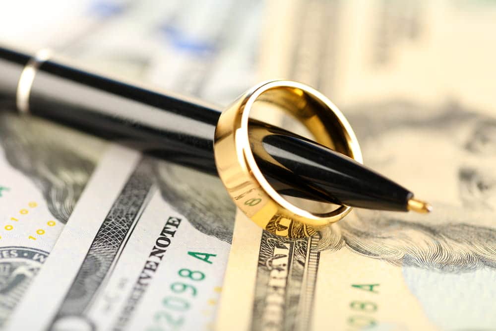 Image is of a wedding ring, pen, and money on legal documents, concept of alimony in South Carolina and financial support.