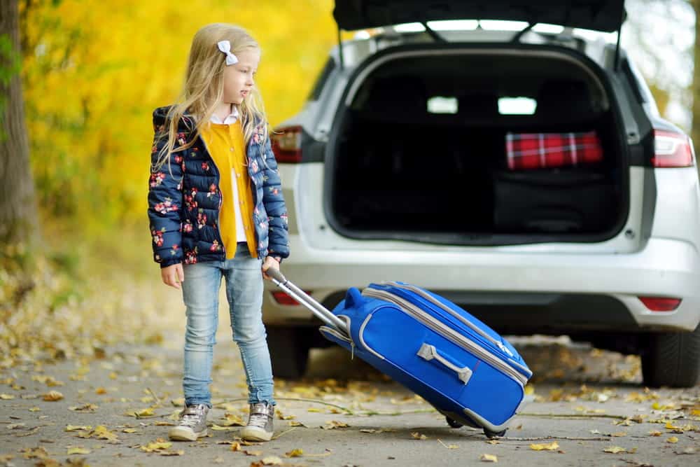 Image is of a child with a suitcase beside a car, representing travel and relocation after a custody order.
