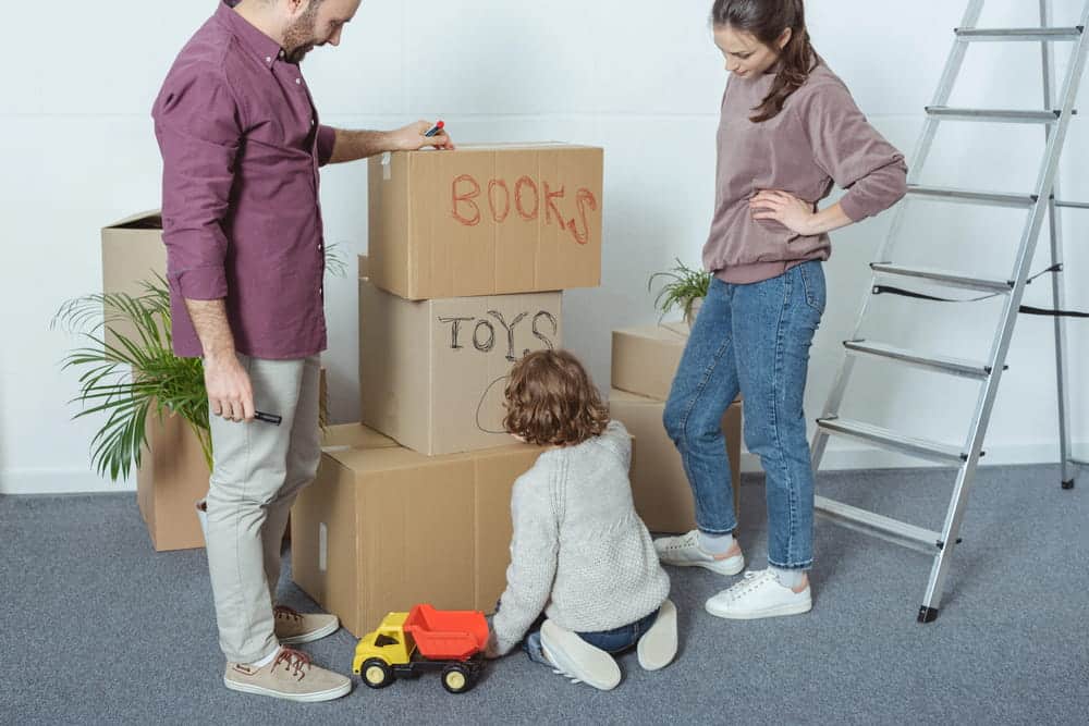 Image is of parents and a child packing moving boxes, concept of family relocation after a custody order.