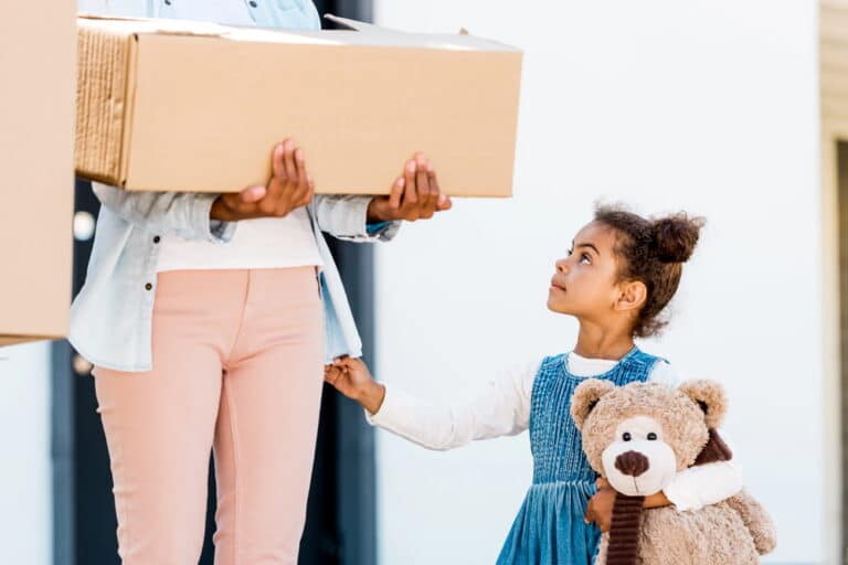 Image is of a parent carrying a moving box while holding a child’s hand, concept of relocation after a custody order.