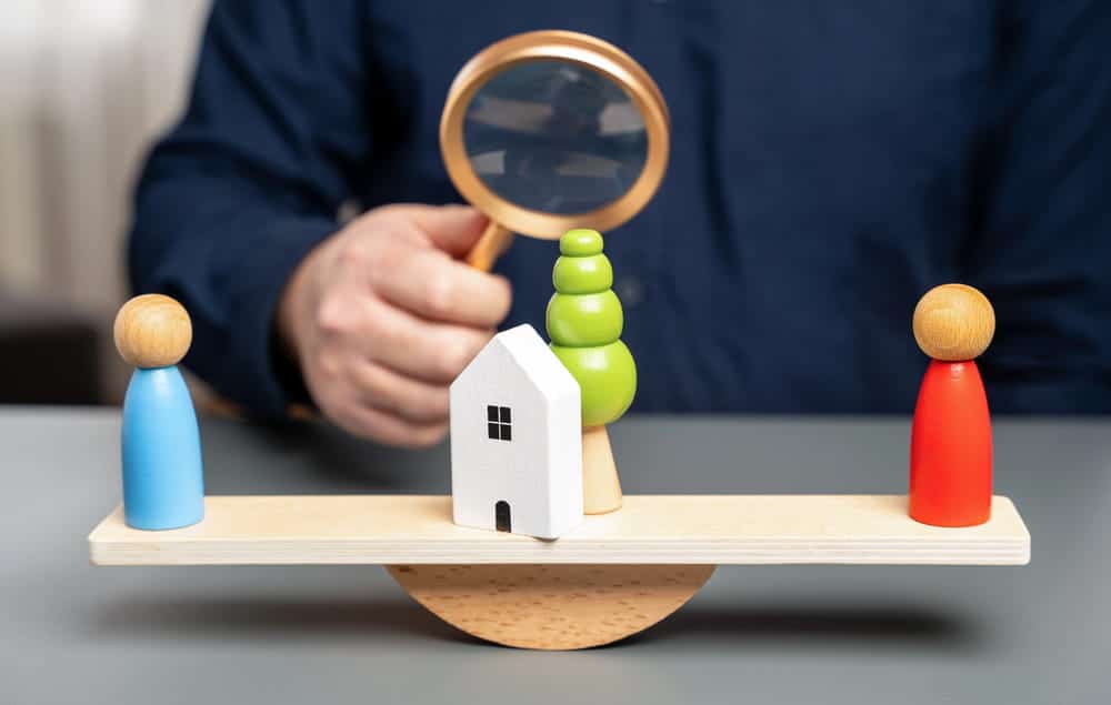 Image is of a house balanced between two people, concept of marital property division in South Carolina.