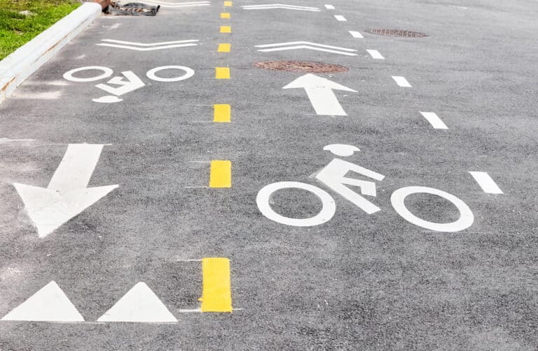 Image is of marked bicycle lanes with directional arrows on a roadway, concept of right of way and proper road positioning for cyclists.