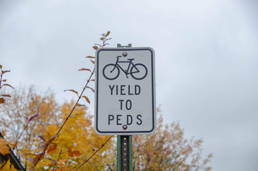Image is of a bicycle yield sign directing cyclists to yield to pedestrians, concept of right of way rules for cyclists.