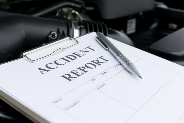 Image is of an accident report form and pen near a vehicle, representing documentation for a motorcycle accident claim.