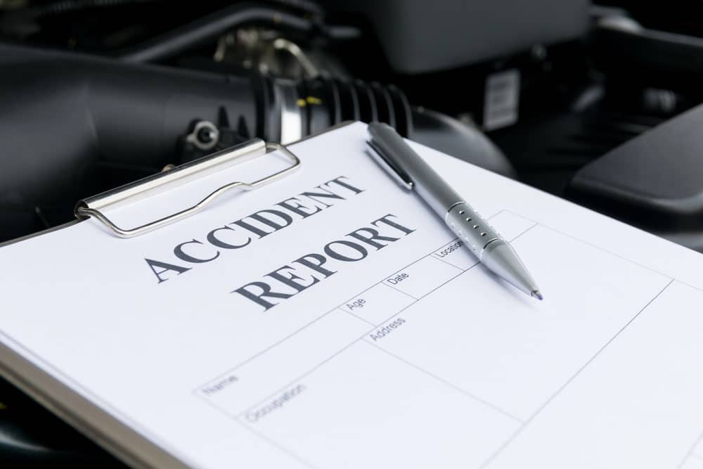 Image is of an accident report form and pen near a vehicle, representing documentation for a motorcycle accident claim.