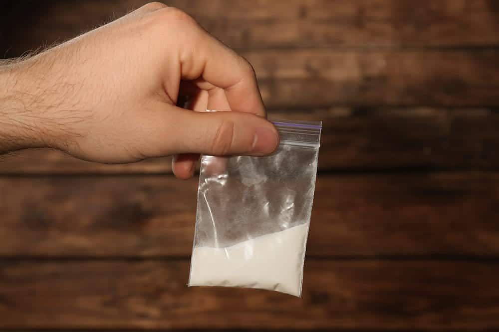 Image is of a person holding a small bag containing white powder, evidence related to intent to distribute in Aiken.