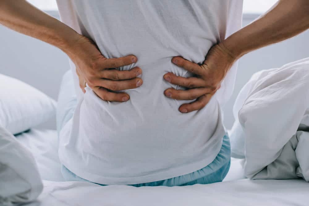 Image is of a person holding their lower back after waking, showing delayed pain after a car accident in Aiken.