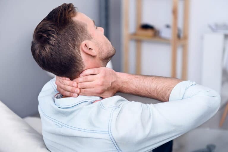 Image is of a man holding his neck in discomfort, showing delayed neck pain after a car accident in Aiken.