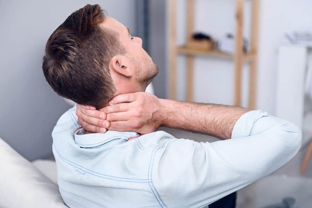 Image is of a man holding his neck in discomfort, showing delayed neck pain after a car accident in Aiken.