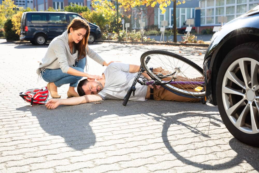 Image is of an injured cyclist lying beside a bicycle and car, concept of injuries from biking in Aiken.