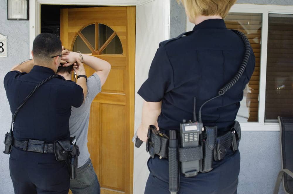 Image is of two police officers detaining a man outside a home, illustrating domestic violence arrests in Aiken.