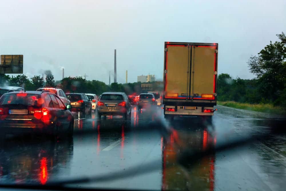 Image shows a commercial truck traveling alongside several vehicles in heavy rain on a wet highway, illustrating the risks of truck accidents in Aiken.
