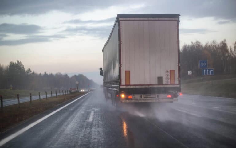 Image shows a large commercial truck traveling on a rain-soaked highway with reduced visibility, illustrating weather-related truck accidents in Aiken.