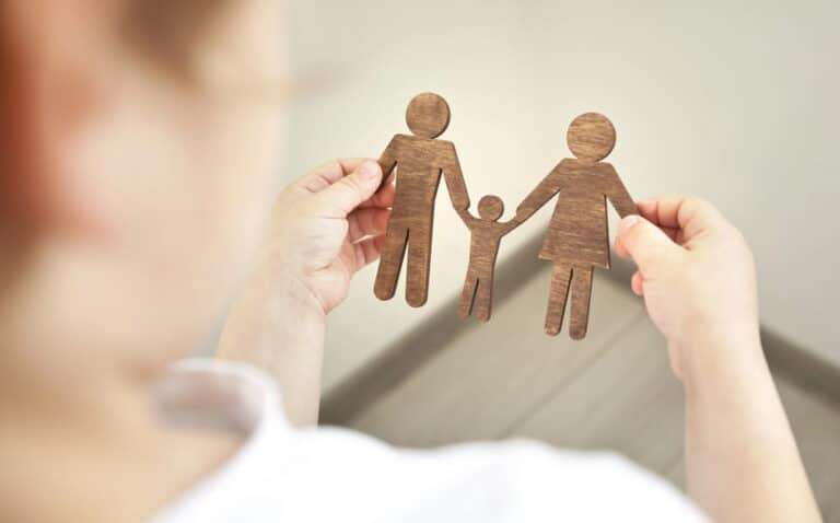Image is of hands holding wooden figures representing two parents and a child, concept of eligibility to adopt a child in South Carolina.